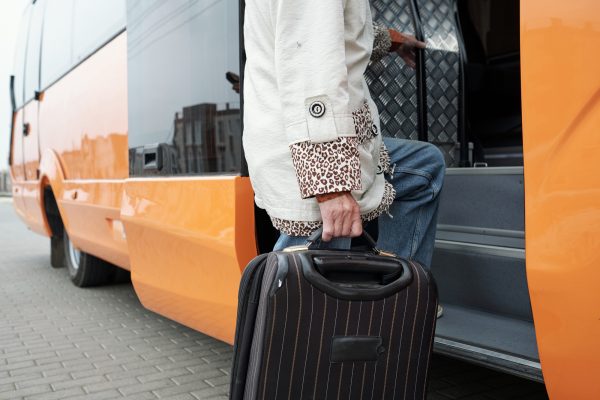 Contemporary senior passenger with suitcase entering bus